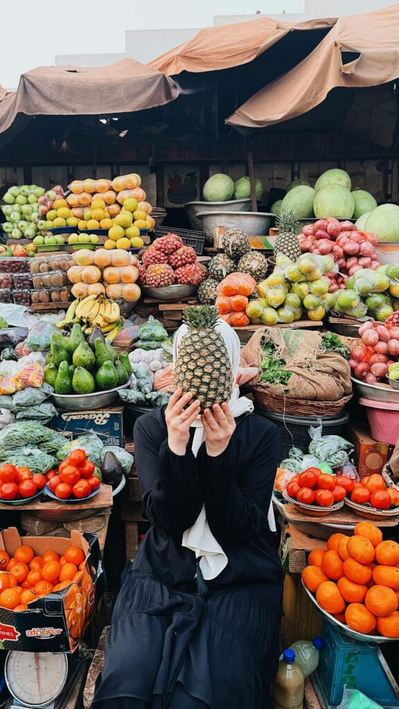 Woman holding a pineapple in a vibrant fruit market in Burkina Faso.
