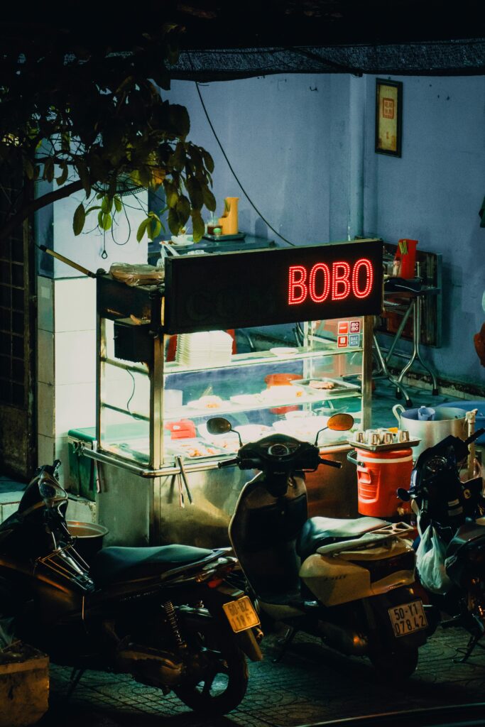 Vibrant street food stall in city at night with motorcycles parked nearby, exuding urban charm.